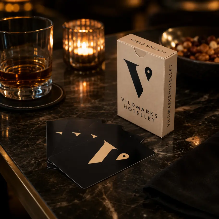 Vildmarkshotellets kortlåda med svarta spelkort, whisky och ljus på mörkt marmorbord.